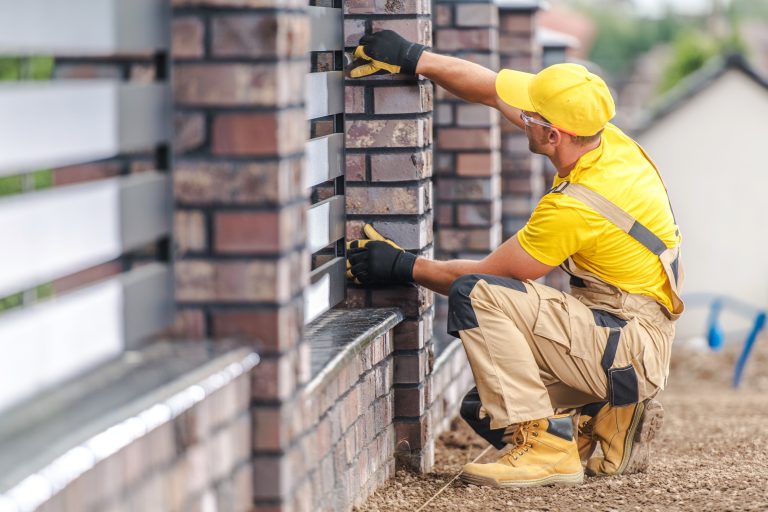 Skilled Worker Laying Bricks on a Modern Fence in a Residential Area During Daylight Hours